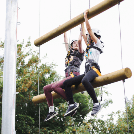 school pupils on a high ropes course with safety harness and hats on