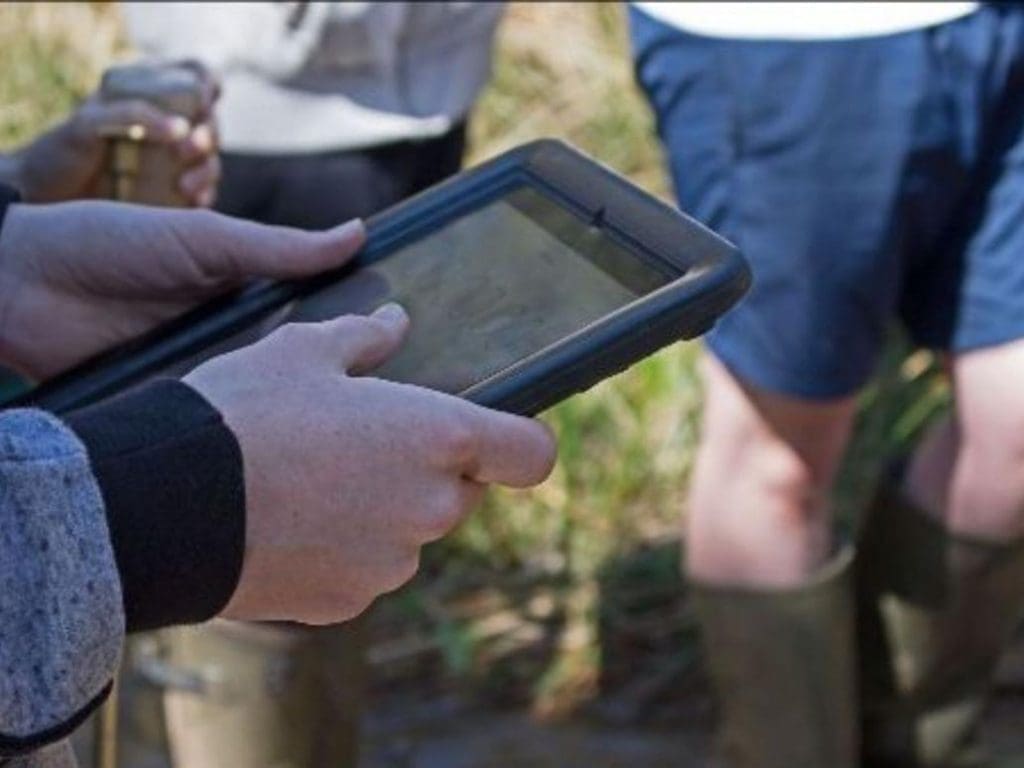 student holding an Ipad in a field outside