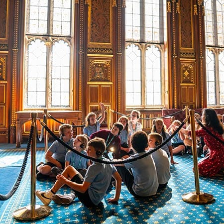 school pupils sitting in a group at the houses of parliament on a school trip