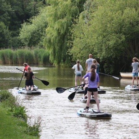 school pupils paddling down a river on paddleboards