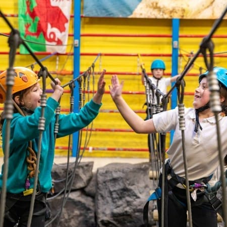 two school pupils high fiving each other on a rope assault course