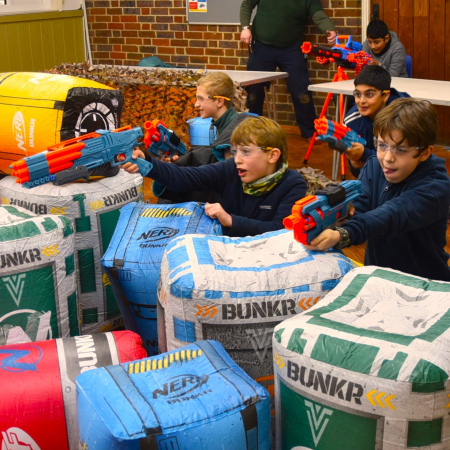 secondary school pupils playing with water rifles outside behind a barricade on a fun school trip