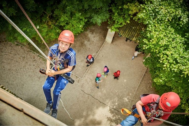 pupils with safety gear and hard hats on a abseiling tower abseiling down