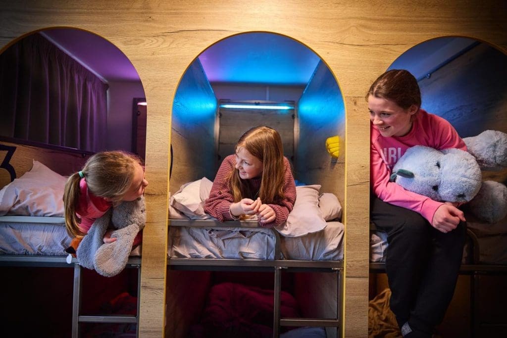 three school pupils in bunk pod style accommodation smiling at one another