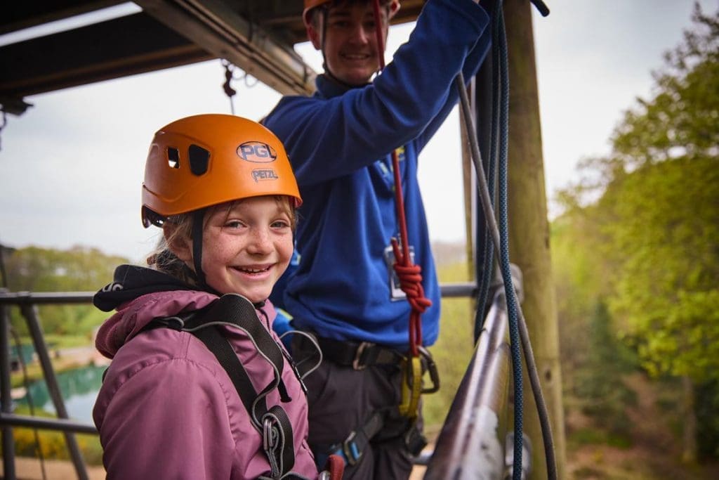 school pupil on top of a zip lining tower with instructor getting ready to zip line down it
