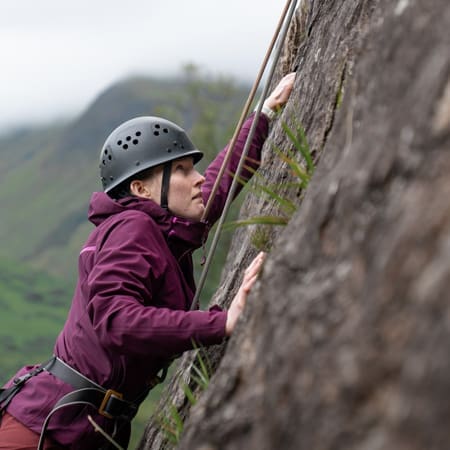 school student in hard hat climbing up a cliff