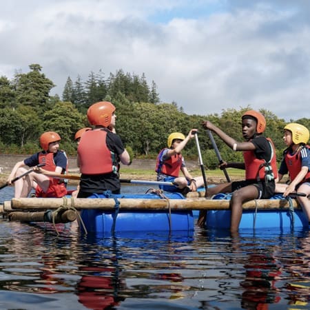 5 secondary school trip pupils in waterproofs on a man made raft on a lake in Scotland