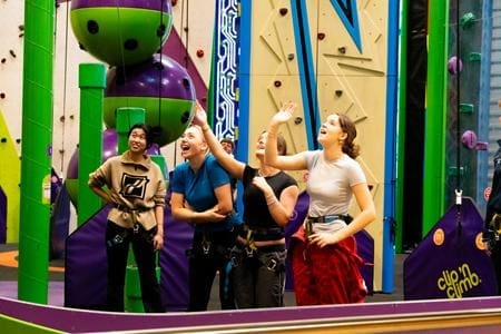 group of school students waving at each other at an indoor climbing centre