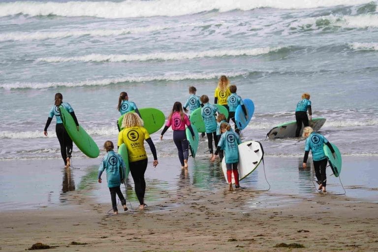 school group at the beach carrying surf boards