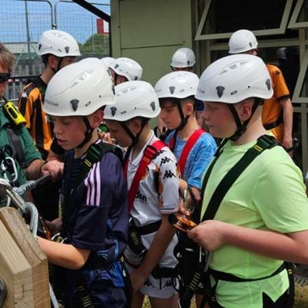 school group with hard hats and safety harnesses doing high ropes