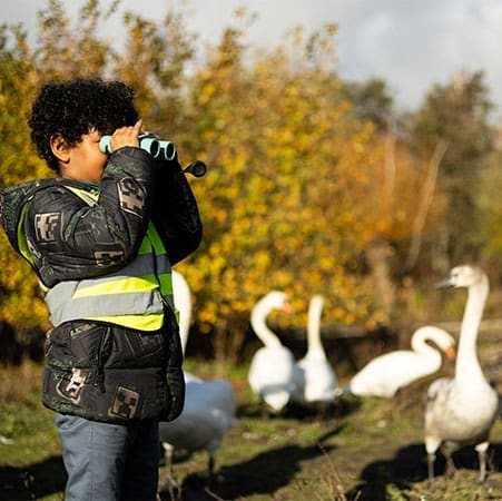 school pupil with binoculars looking at bird types in a river