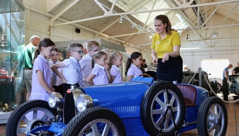 primary pupils with tour guide looking at a blue classic car